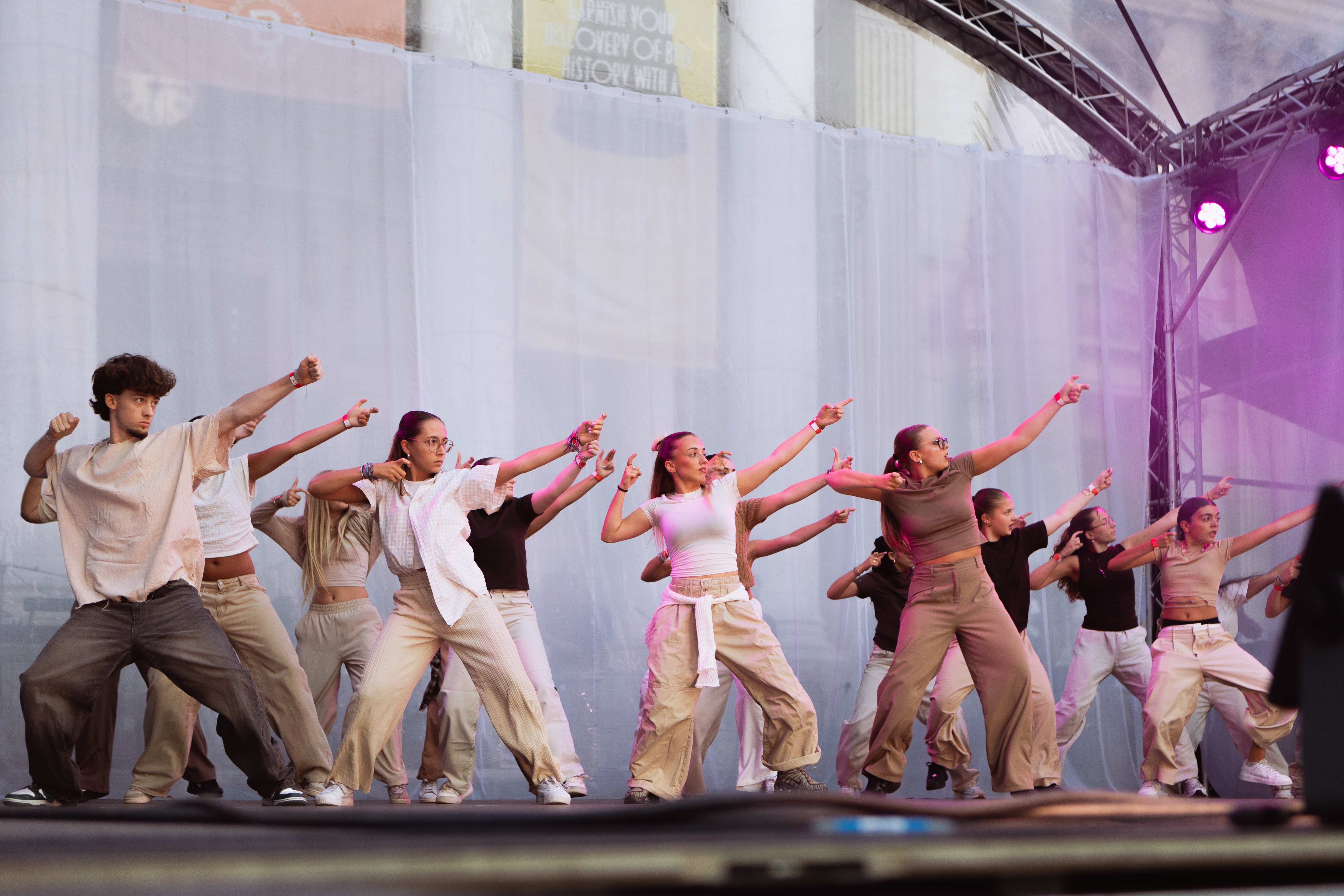 A group of hip-hop dancers in casual outfits with arms extended in perfect synchronisation on an outdoor stage at Brussels Dance Festival