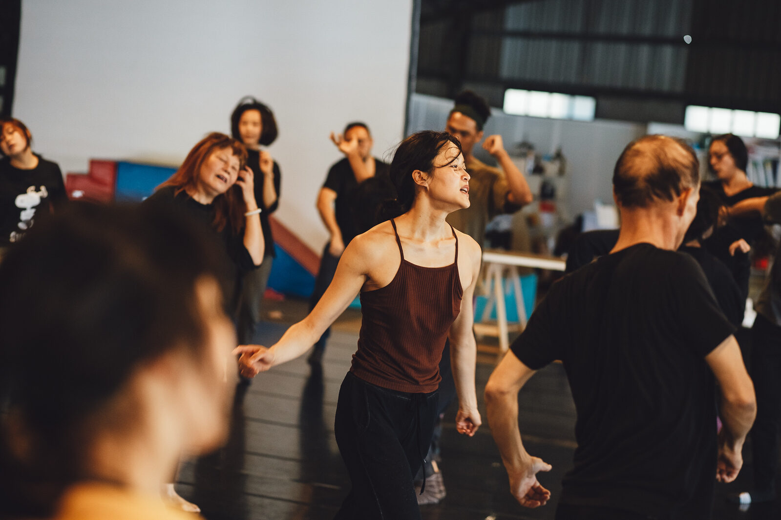 Dancers of different ages moving through a contemporary dance improvisation workshop in a large studio space.