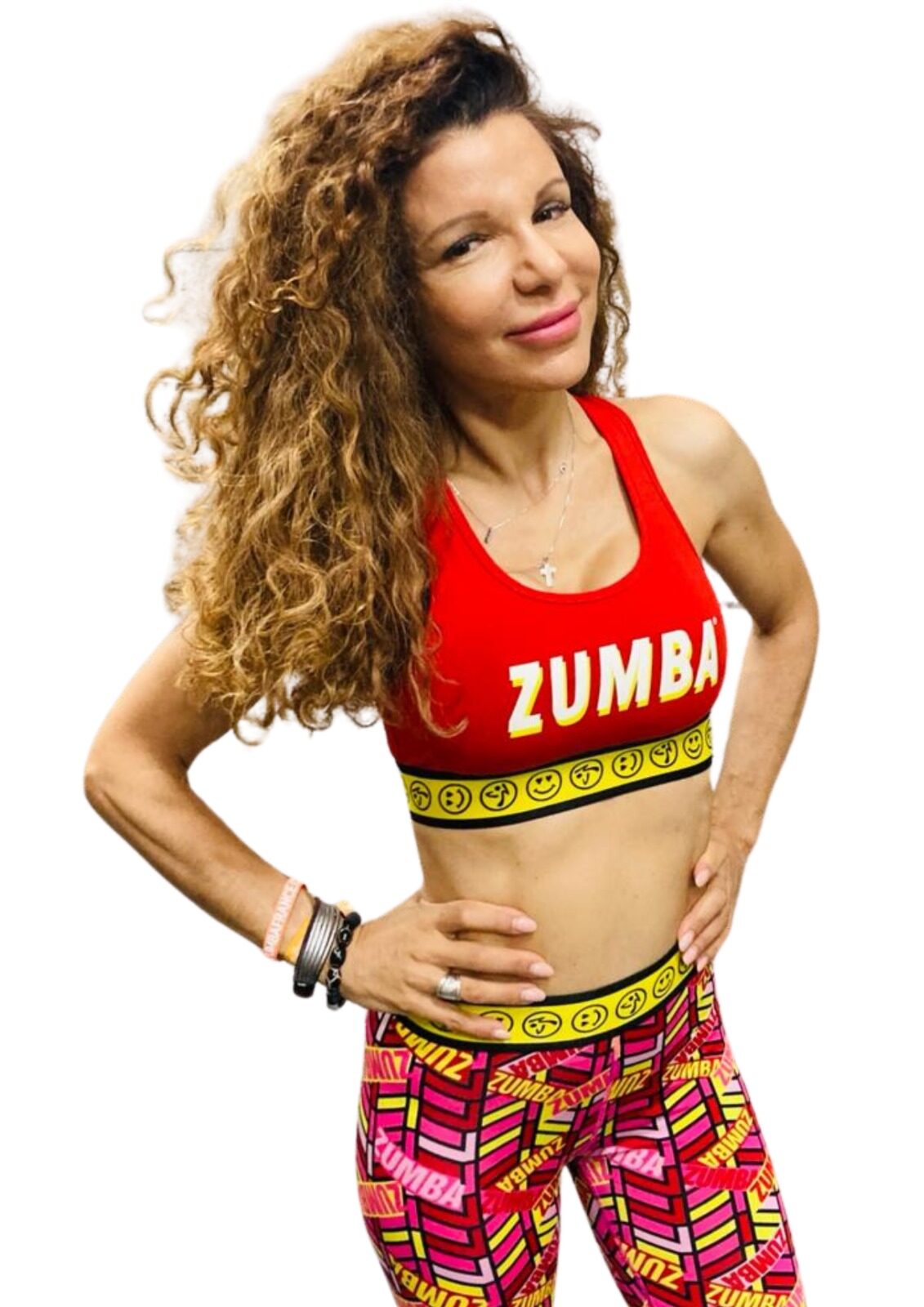 A smiling woman with curly hair posing in a red and yellow Zumba-branded outfit.