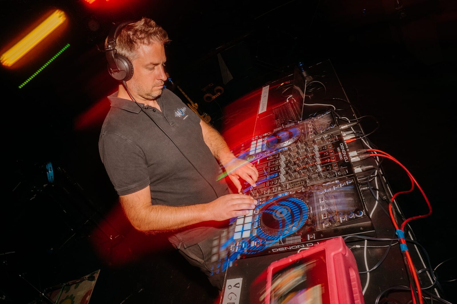 A DJ wearing headphones mixing on a Denon DJ controller under red stage lighting.