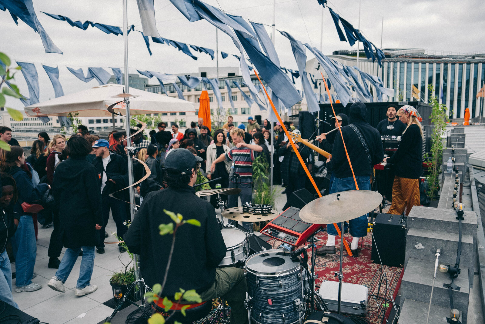 A live band performing on a rooftop terrace strung with blue fabric banners, a crowd gathered around them.